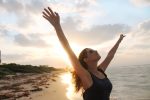 Femme qui lève les bras en l'air sur la plage au coucher du soleil